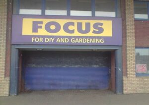 Wide blue garage door with a yellow sign above that reads Focus for DIY and Gardening