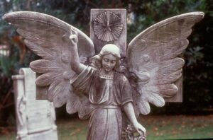 A statue of an angel with an uplifted arm. Its wings are spread wide open. Surrounding tombstones are also visible.